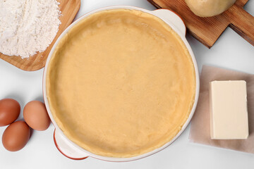 Pie tin with fresh dough and ingredients on white background, flat lay. Making quiche