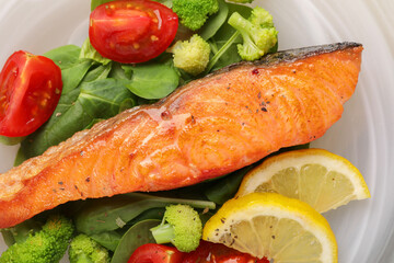 Healthy meal. Piece of grilled salmon, vegetables, lemon and spinach on plate, top view