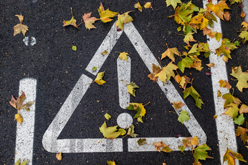 detail of undetermined danger sign painted on the ground between dry leaves