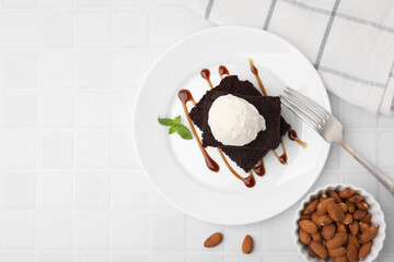 Tasty brownies served with ice cream and caramel sauce on white tiled table, flat lay. Space for text