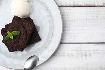 Tasty brownies served with ice cream and mint on white wooden table, top view. Space for text