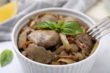 Delicious fried chicken liver with onion and basil in bowl on white table, closeup