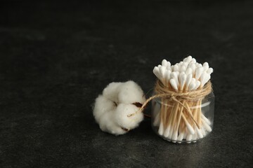 Cotton swabs and flower on black table, space for text