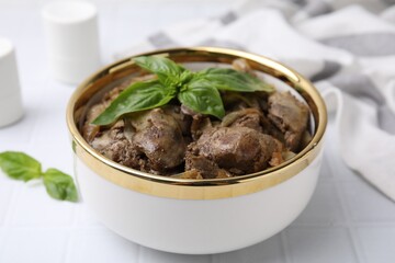 Delicious fried chicken liver with onion and basil in bowl on white tiled table, closeup