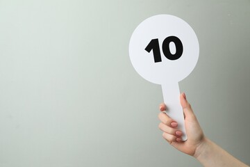 Woman holding auction paddle with number 10 on light grey background, closeup. Space for text