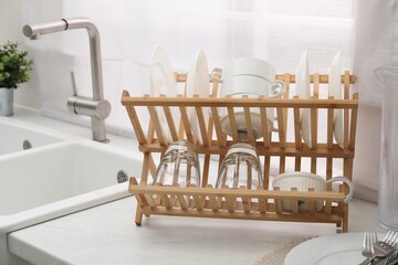 Fototapeta na wymiar Drying rack with clean dishes on light marble countertop near sink in kitchen