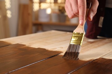 Man with brush applying wood stain onto wooden surface indoors, closeup. Space for text
