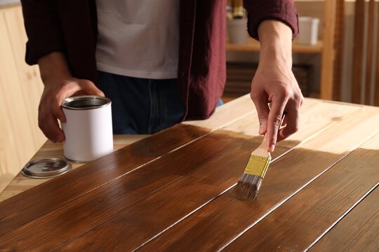 Man with brush applying wood stain onto wooden surface indoors, closeup