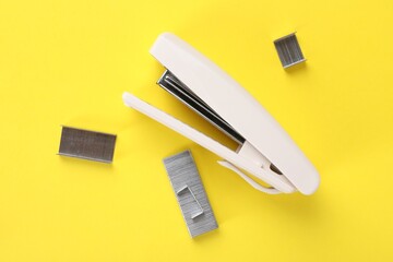 White stapler with staples on yellow background, flat lay