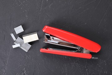 Red stapler with staples on black textured table, flat lay