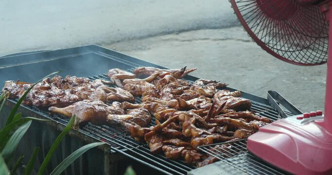 Close up of a barbecue fan activating the fire to grill chicken thighs faster.