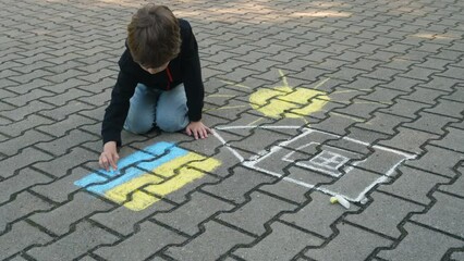 Child Draws With Chalk on Pavement Drawing of House, Sun and Ukrainian Flag. Little Boy Drawing Ukrainian Flag With Chalk. Crisis, Peace, Stop Aggression, Children Against War. Freedom to Ukraine.