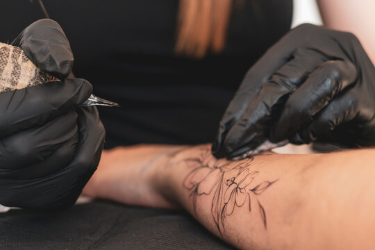 a gorgeous tattoo of a flower on woman's hand, tattoo artist in the process of work