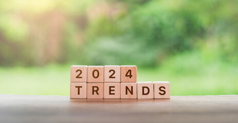 concept of ‘New Year, 2024, trends’ through wooden blocks spelling out ‘2024 TRENDS’. Set against a blurred green background on a wooden surface. - obrazy, fototapety, plakaty