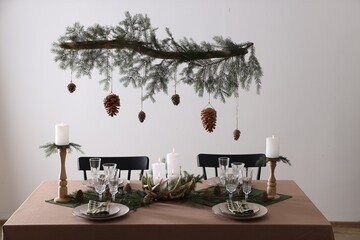 Christmas celebration. Cones hanging from fir tree branch over table with burning candles and tableware