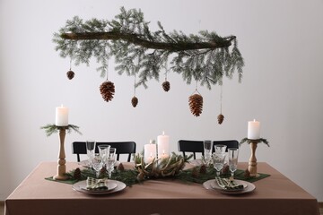 Christmas celebration. Cones hanging from fir tree branch over table with burning candles and tableware