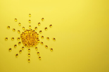 Vitamin D concept, nutritional supplement and health. Yellow capsules in form of the sun on yellow...