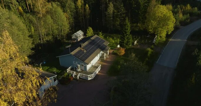 Aerial view around a tree, revealing a house with solar cells, fall evening