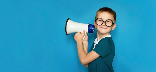 funny child on an isolated blue background shouts into megaphone to announce something, pointing...