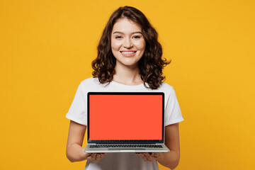 Young IT woman wears white blank t-shirt casual clothes hold use work on blank screen workspace area laptop pc computer isolated on plain yellow orange background studio portrait. Lifestyle concept.