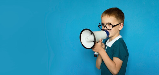 funny child on an isolated blue background shouts into megaphone to announce something, pointing...