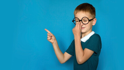 photo of smiling happy boy pointing his finger towards the place to copy, highlighted on a simple background. Back to school. Funny kid with glasses from elementary school. Education