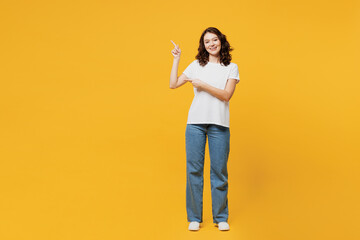 Full body young woman she wearing white blank t-shirt casual clothes point index finger aside indicate on workspace area isolated on plain yellow orange background studio portrait. Lifestyle concept.