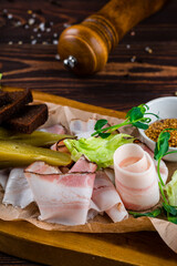 Fresh slices of bacon, pickles, garlic croutons, lettuce, French mustard and herbs on a wooden...
