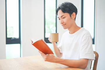 自宅のリビングで読書をする若い男性 - obrazy, fototapety, plakaty