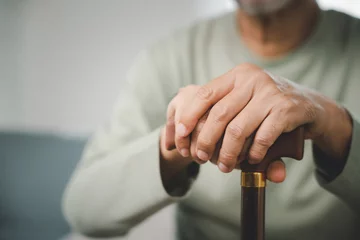 Foto op Canvas Close up hands of Asian Elderly hand holding handle of cane, senior disabled man holding walking stick, Old man sitting resting at home hold wooden walking cane, International Day for the Elderly © sorapop