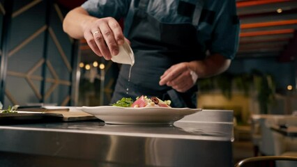 A chef holds a cup of oil and dresses a bruschetta with it in the kitchen of an Italian restaurant