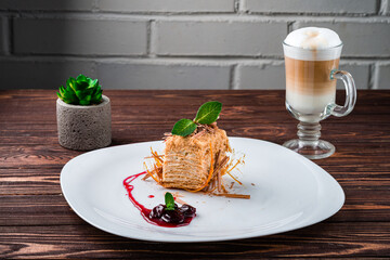 Slice of classic layer cake Napoleon with cherry jam, mint and a cup of latte.