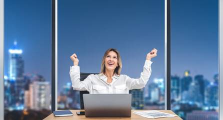 Smiling businesswoman is raising hands sitting in office room, panoramic window