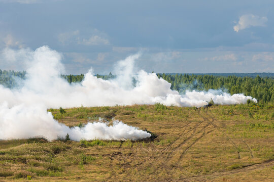 Heavy combat vehicles tanks drive around the butts and put up a smoke screen