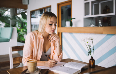 Young woman sitting at table and writing in notebook in cafe