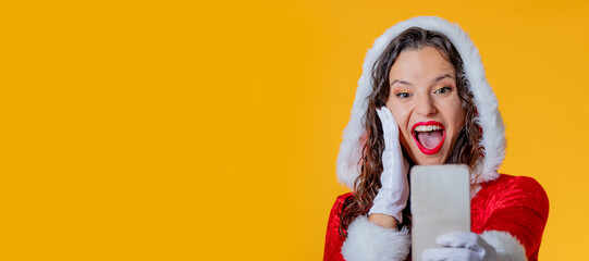 young woman in santa claus costume isolated using mobile phone or smartphone - obrazy, fototapety, plakaty