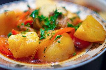 Stewed potatoes with carrots and onions in tomato sauce in a plate. Ready homemade vegetarian dish. Selective focus