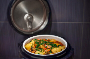 Delicious vegetable stew with potatoes and herbs in tomato sauce in a slow cooker with an open lid in the kitchen, selective focus