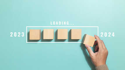 Hand putting wood cube for countdown to 2024 with download bar. Loading year 2023 to 2024. Start...