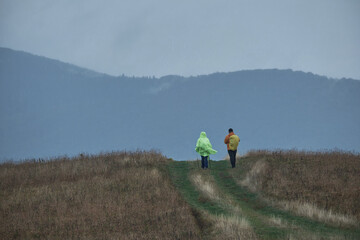 A couple of tourists are walking in the mountains in the rain. Autumn hiking in bad weather