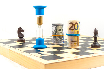 Front angle view of chess board with two black chess pieces, an hourglass with falling sand within...