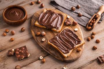 Board of bread with chocolate paste and hazelnuts on wooden background