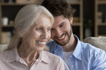 Close up of happy mature woman sit on couch with caring young adult grown up son. Loving millennial man enjoy priceless time with smiling elderly mother. Multigenerational family ties, love and care