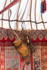 Traditional Asian wooden bow with arrows hanging on the felt wall of a yurt - the home of nomads