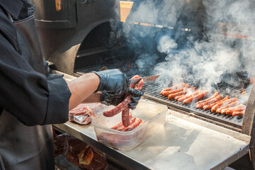 Process of preparing hot dog sausages on a grill with burning coals. Street eatery - obrazy, fototapety, plakaty