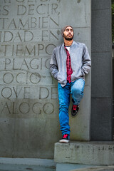 Caucasian guy in red, casual outfit, full-body shot, leaning on park wall.