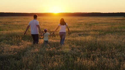 Mother, father, child dream together in park at sunset. Family run on green grass in meadow. Happy family, child, walk through summer field, holding hands. Mom dad daughter walks together in nature.