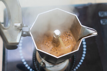 Chimney of stove-top moka pot is flinging out crema espresso coffee and also has smoke steam or...