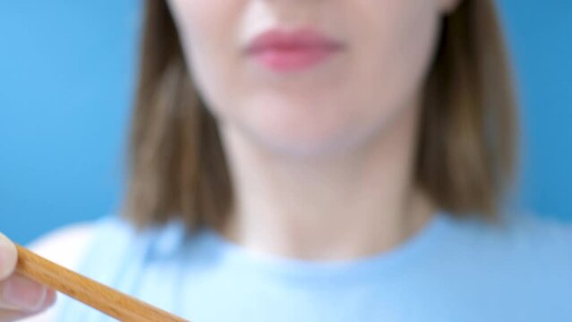 Young woman using wooden chopsticks eating Japanese natto beans front view close-up on blue background.