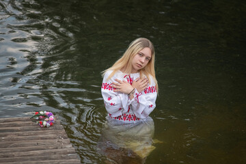 A young beautiful blonde girl in a national costume in the river.